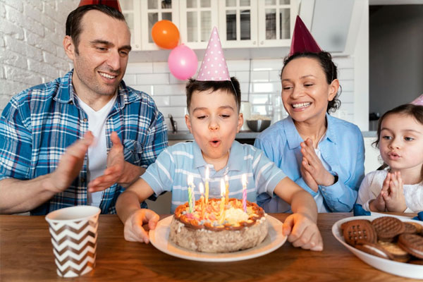 Cậu bé đội mũ tiệc thổi nến bên bố mẹ trong buổi chúc mừng sinh nhật con trai