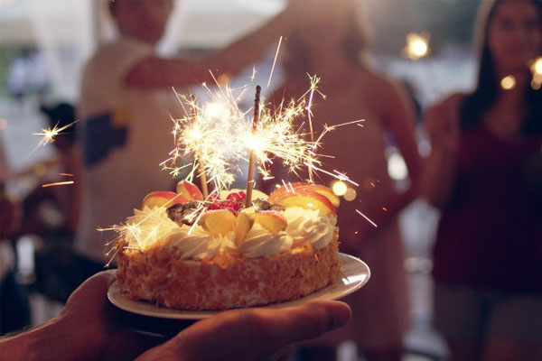Bánh kem trái cây cắm pháo que sáng lấp lánh được nâng lên giữa buổi tiệc tối